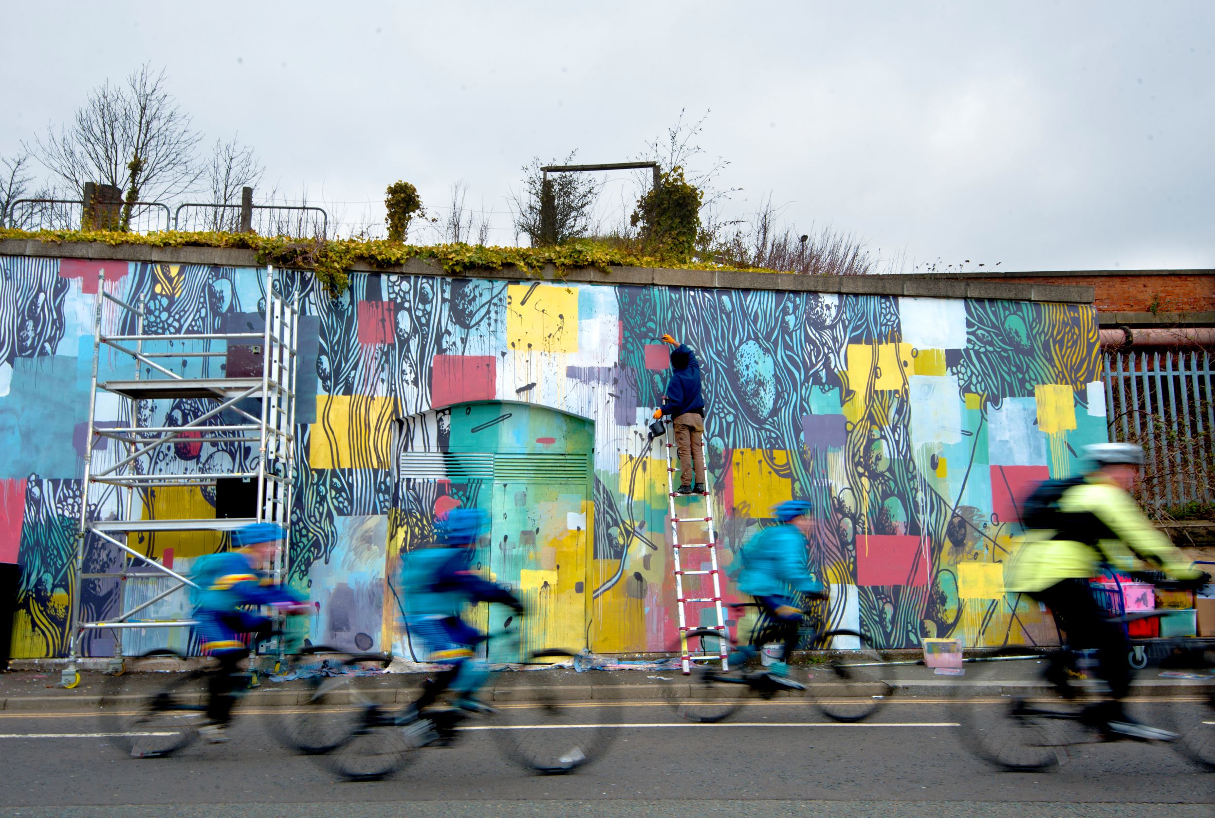 Cyclists ride past a rural mural